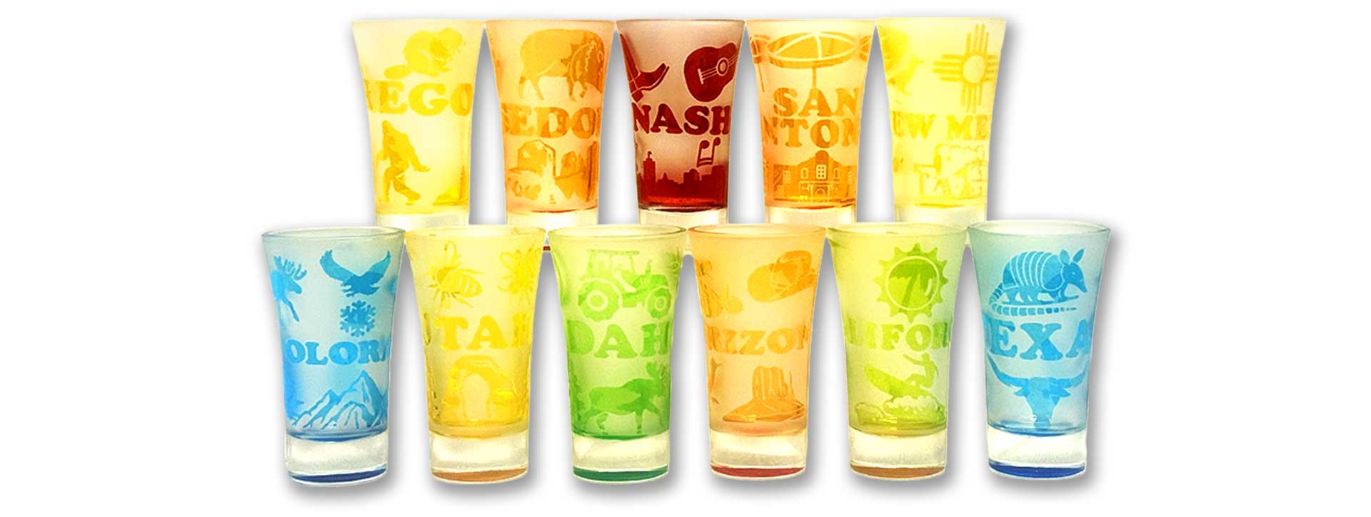 A wholesale display of frosted, multi-colored custom tall cordials featuring wrap-around state souvenir designs with iconic landmarks and wildlife graphics