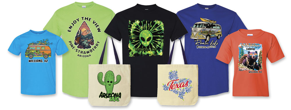 A wholesale display of custom screen-printed t-shirts and tote bags featuring colorful regional souvenir designs like Route 66, Arizona, Roswell, and Texas themes