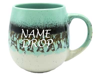 A wholesale round ceramic souvenir mug with a speckled mint green, dark brown, and cream reactive drip glaze finish featuring a script NAME DROP text placeholder